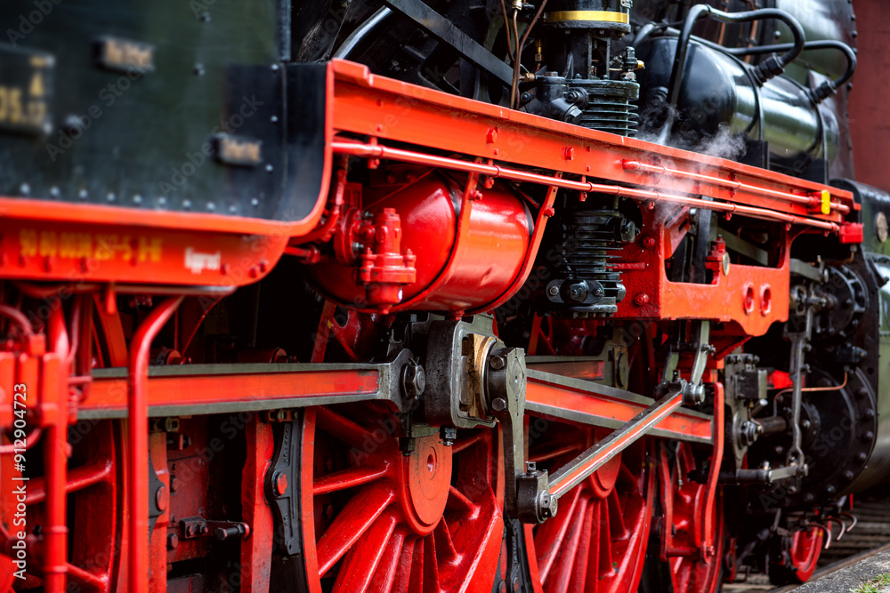 Large cast-iron flywheels from a functioning historic German steam locomotive. Red painted spokes and connecting rods and oiled bare steel. Railroad technology from bygone times that still inspires. Large cast-iron flywheels from a functioning historic German steam locomotive. Red painted spokes and connecting rods and oiled bare steel. Railroad technology from bygone times that still inspires.