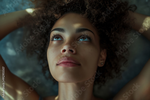 A woman with curly hair lies down, looking contemplatively upwards with a soft, thoughtful expression on her face.