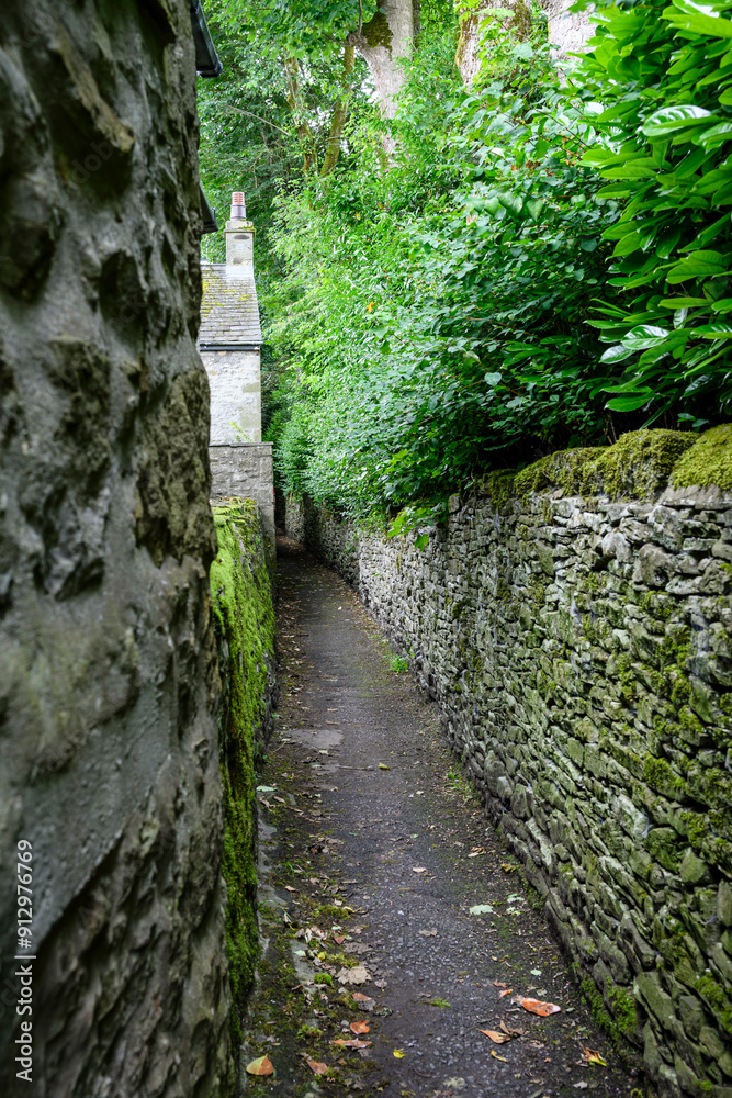 Narrow stone pathway surrounded by lush greenery and old walls. Narrow stone pathway surrounded by lush greenery and old walls.
