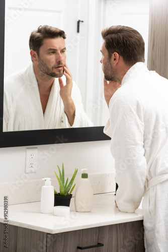 A man is applying lotion to his face in front of a mirror. Concept of self-care and personal grooming