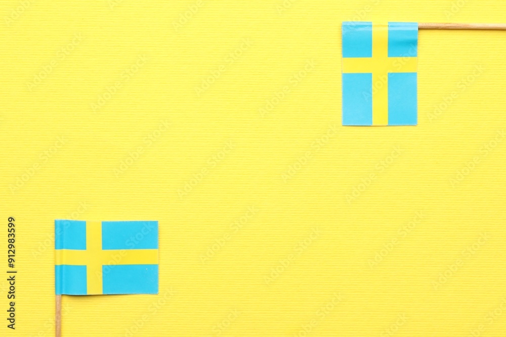 Obraz premium Small paper flags of Sweden on yellow background, top view. Space for text