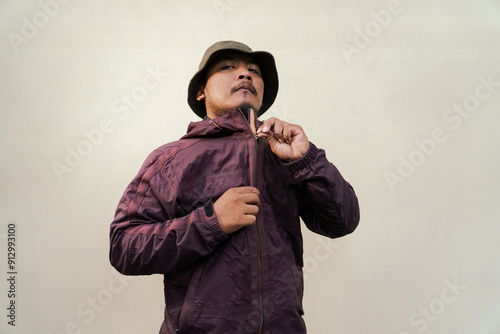 Half body portrait of adult Asian man with beard and mustache posing in various styles. Mature man wearing adventure outfit with jacket and bucket hat isolated on beige background.