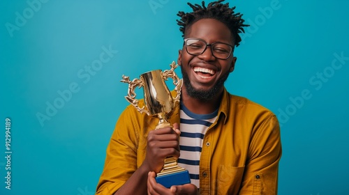 Happy male African American student boy raising a golden trophy posing in front of blue background with copy space, concept of winning, top prize, award winning prize. photo