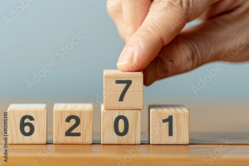 A hand is holding wooden blocks that spell out the numbers 2, 7, and 1. The blocks are stacked on top of each other, creating a sense of progression and accomplishment. Concept of setting goals