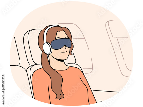 Woman passenger of flight with blindfold and earphones sleeps in airplane chair sitting outside porthole. Young girl first class passenger flies on business trip on airplane and smiles
