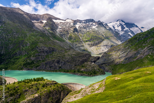 An idyllic landscape of snow capped peaks, mountains covered with green grass and a blue lake. Grossglockner, the highest mountain in Austria. Hohe Tauern National Park