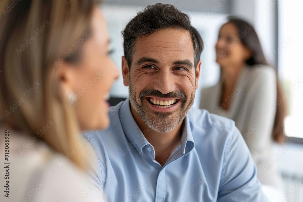 A man with a big smile is sitting in front of two women. The man is wearing a blue shirt and the women are smiling. Scene is happy and friendly A man with a big smile is sitting in front of two women. The man is wearing a blue shirt and the women are smiling. Scene is happy and friendly