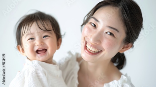 Studio photo of an Asian mother and her smiling baby, both radiating warmth and affection.