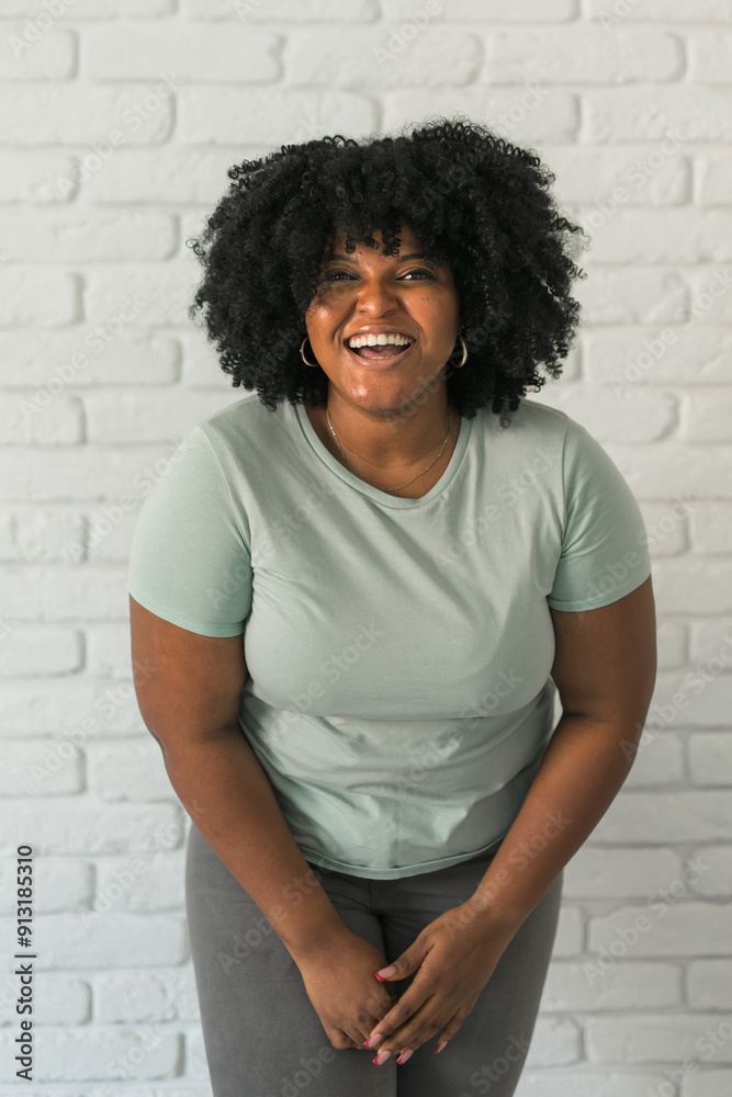 Laughing millennial African American woman with an afro hairstyle and good sense of humor smiling and laugh on brick wall at home background. Copy space. Happiness and good emotions concept Laughing millennial African American woman with an afro hairstyle and good sense of humor smiling and laugh on brick wall at home background. Copy space. Happiness and good emotions concept