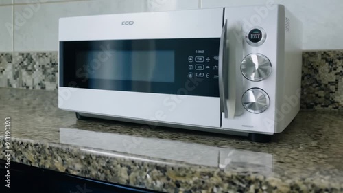 A microwave sits on a countertop. The microwave is white and has a silver handle. The countertop is made of granite and has a shiny, reflective surface