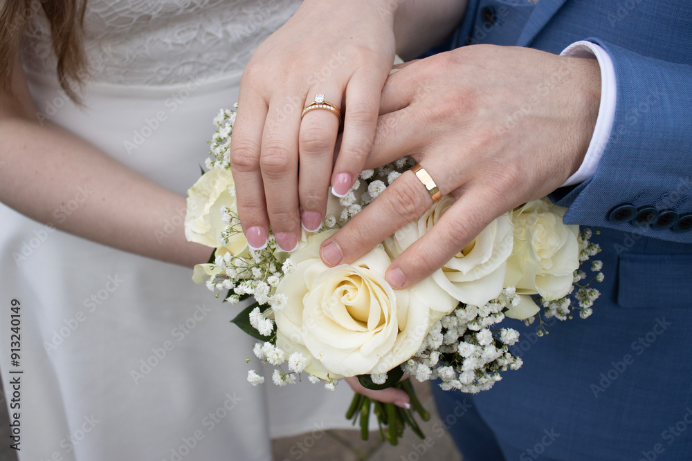 Bride and groom holding hands on wedding bouquet. Wedding rings close-up. White roses at wedding Bride and groom holding hands on wedding bouquet. Wedding rings close-up. White roses at wedding