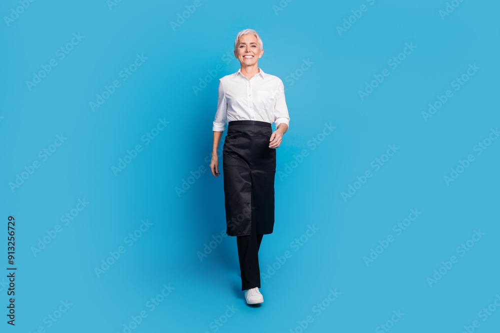 Full size photo of pretty retired female walking barista small coffee shop owner wear waitress uniform isolated on blue color background