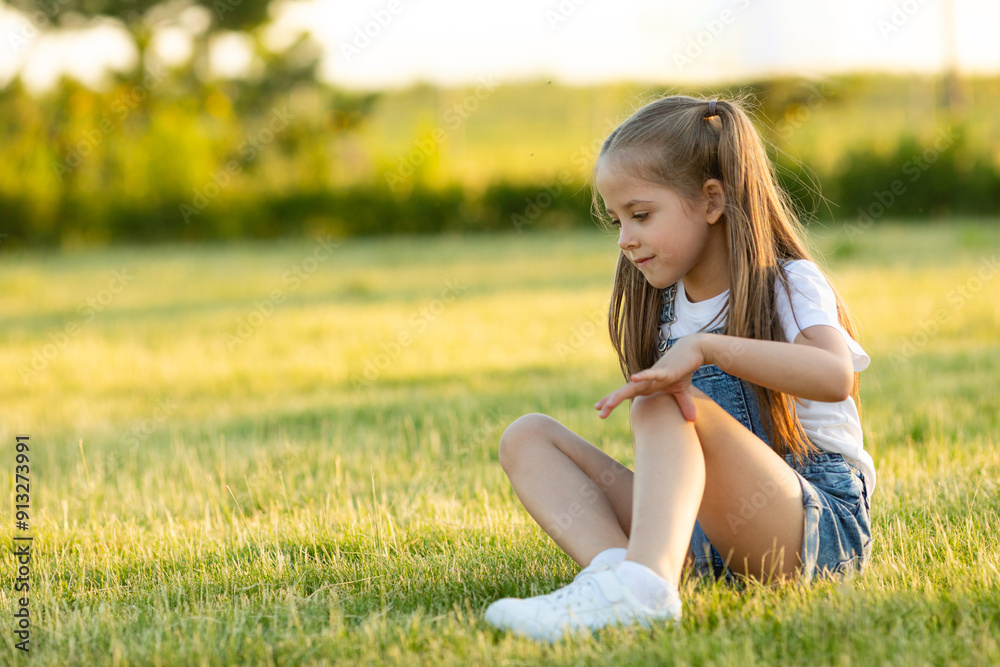 Happy little girl sitting on grass and smiling. Perfect for innocence and joy of childhood concept. Ideal for use in advertisements, blog or any content related to children, nature. High quality photo