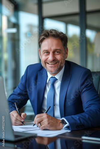 A middle-aged, bearded, gray-haired lawyer sits at his desk using a computer smiling and looking at the camera.