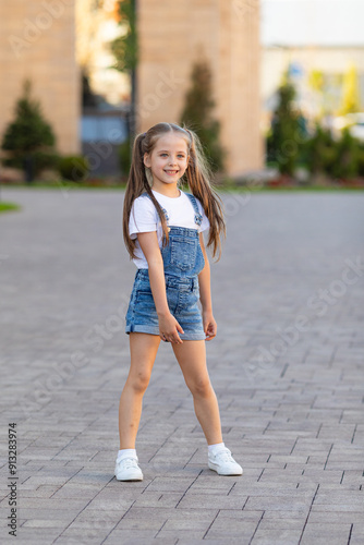 Smiling little girl is having fun walking down the street. Urban lifestyle concept. City background.