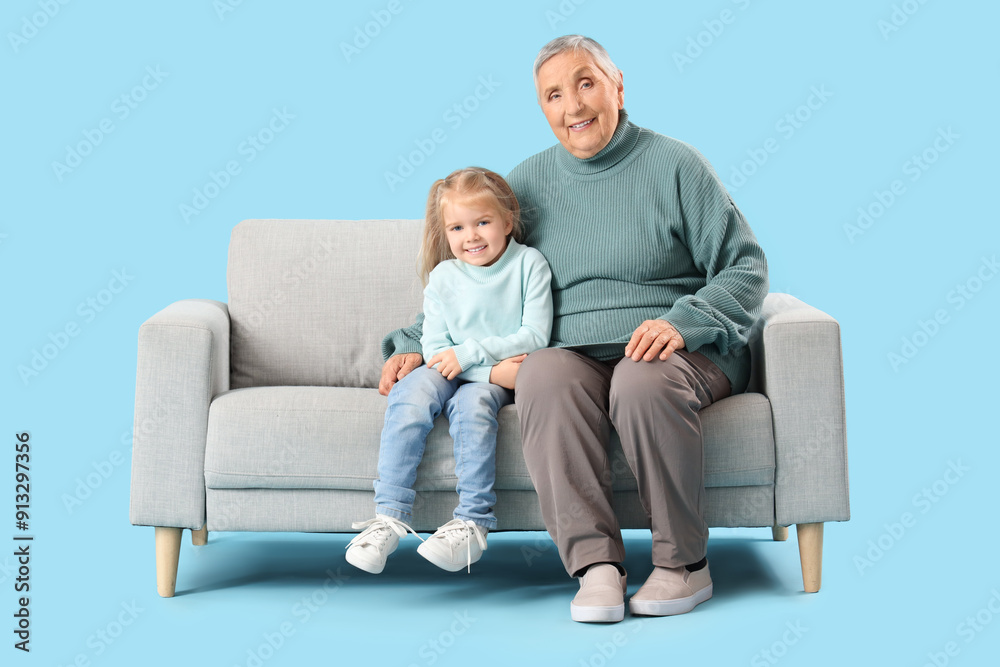 Cute little girl with her granny sitting on sofa against blue background Cute little girl with her granny sitting on sofa against blue background