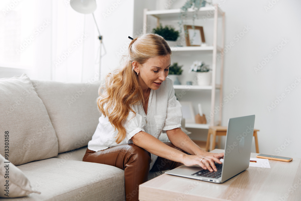 Woman working remotely from home, sitting on a cozy couch, focused on typing on her laptop and looking at the screen Woman working remotely from home, sitting on a cozy couch, focused on typing on her laptop and looking at the screen