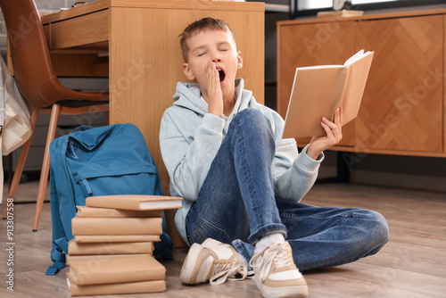 Tired teenage boy with book yawning in library