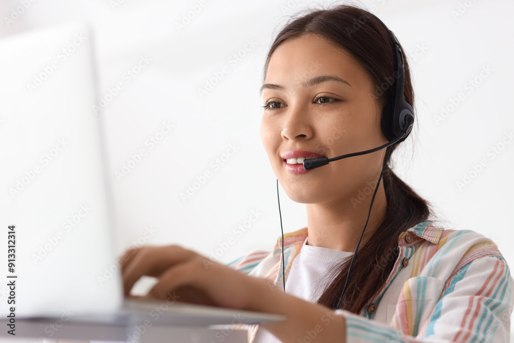 Young female receptionist in headset working with modern laptop in office