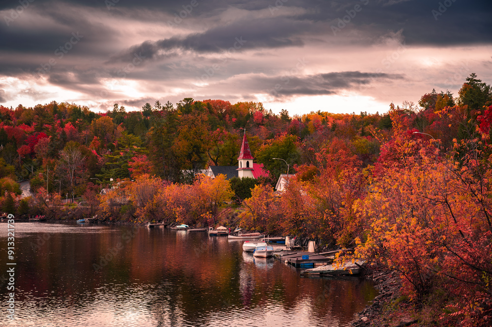 Fototapeta premium Autumn in picturesque village of Wakefield, boats on the Gatineau River, red church steeple, colourful foliage fall season, dramatic sky cloudscape, La Peche, Outaouais, Quebec, Canada, October 2022