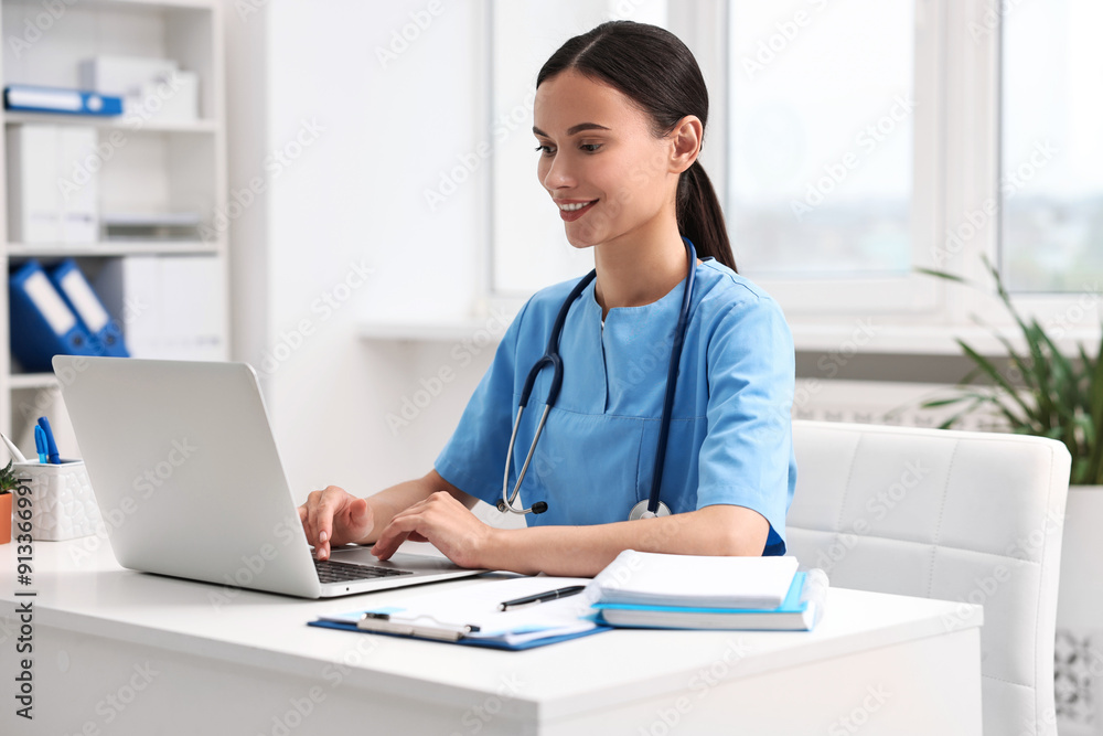 Smiling nurse working with laptop at table in clinic Smiling nurse working with laptop at table in clinic