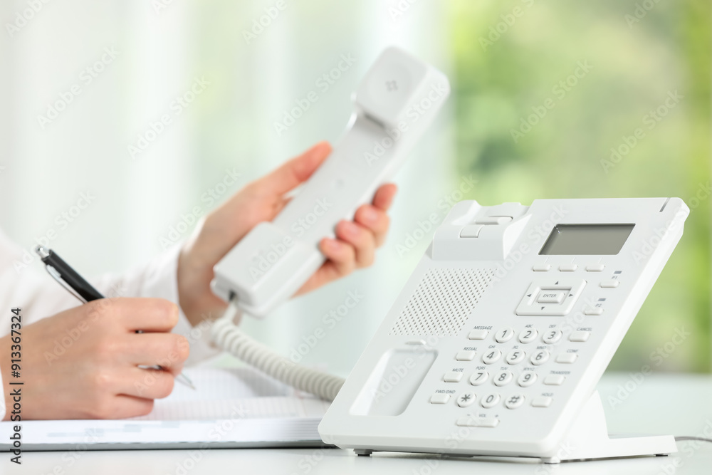 Assistant with telephone handset writing at white table against blurred background, closeup Assistant with telephone handset writing at white table against blurred background, closeup