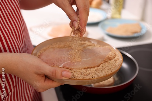 Woman holding raw schnitzels with breadcrumbs in kitchen, closeup photo