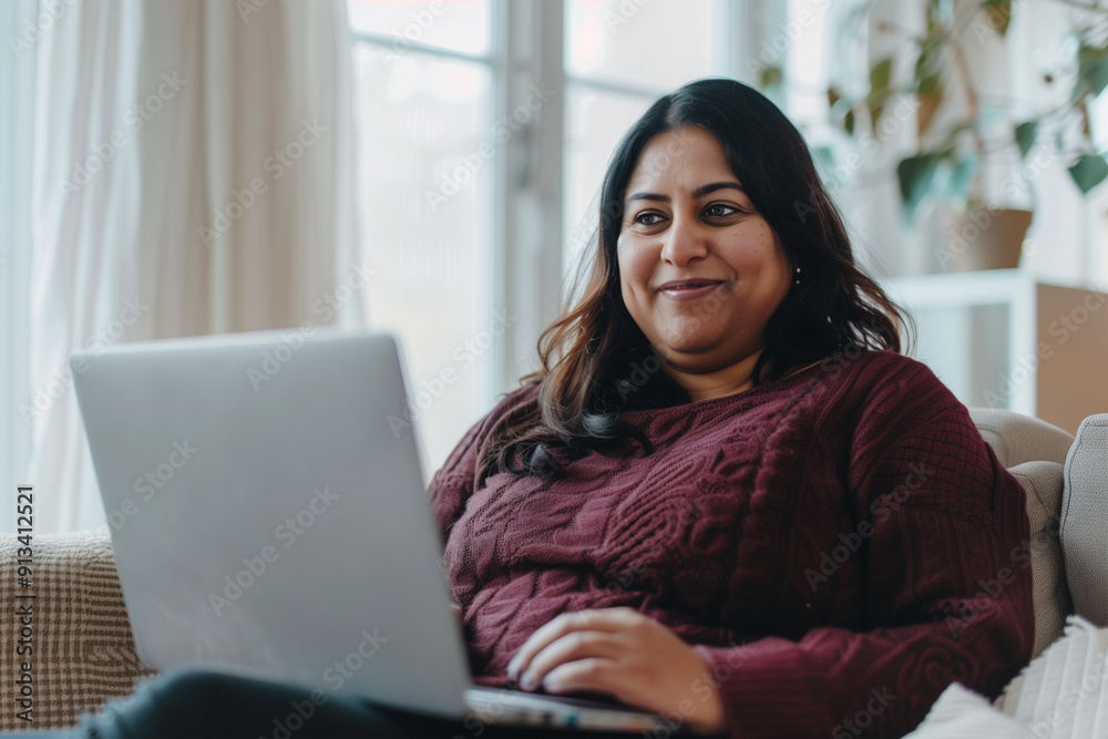 An overweight Indian businesswoman sitting at a laptop smiling and looking at a computer screen.
