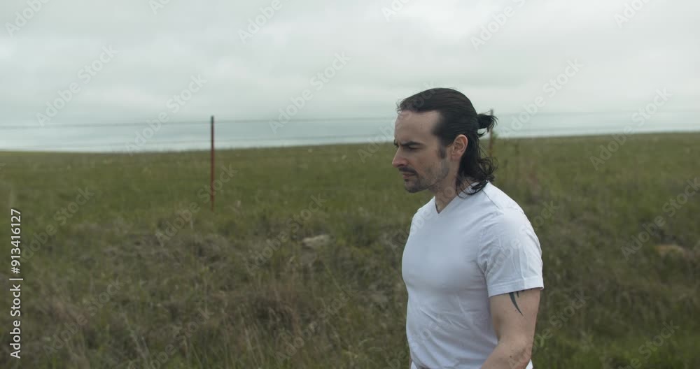 Man walking on dirt road by expansive fields. The overcast sky adds a moody atmosphere as he moves with determination, dressed in casual attire, embodying a sense of solitude and reflection. Man walking on dirt road by expansive fields. The overcast sky adds a moody atmosphere as he moves with determination, dressed in casual attire, embodying a sense of solitude and reflection.