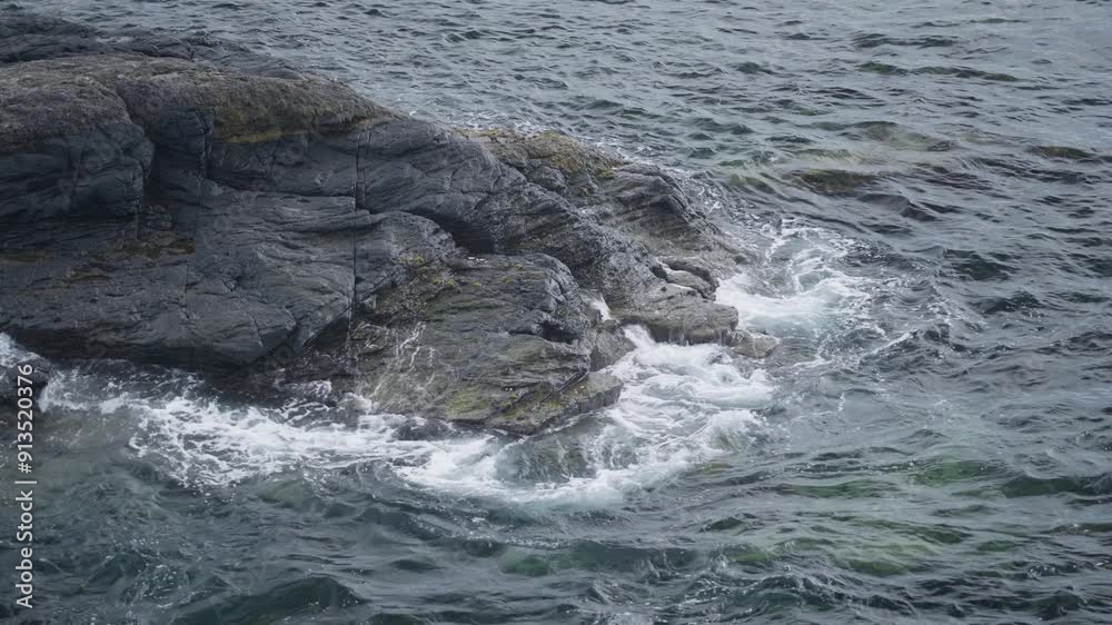 Waves crashing against rugged rocks on a calm coastal day Waves crashing against rugged rocks on a calm coastal day