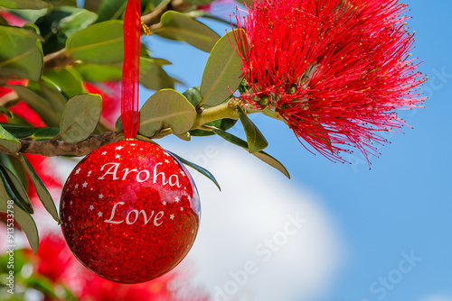 A shiny red Christmas bauble hanging in a Summer flowering New Zealand Pohutukawa tree. 