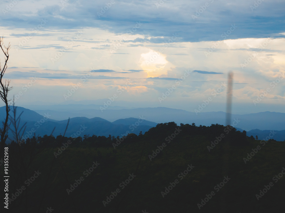 Fototapeta premium Mountains under a cloudy sky at sunset. Lush greenery in the foreground contrasts beautifully with the misty distant mountains. Serene view of Phu Soi Dao National Park in Thailand.