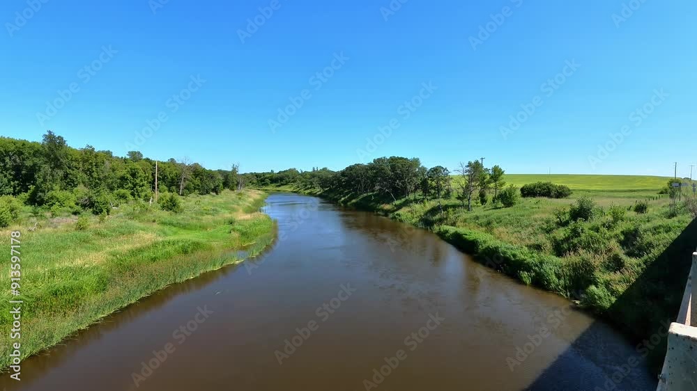 Aerial view of a calm, muddy river flowing through a lush green landscape under a clear blue sky. Aerial view of a calm, muddy river flowing through a lush green landscape under a clear blue sky.