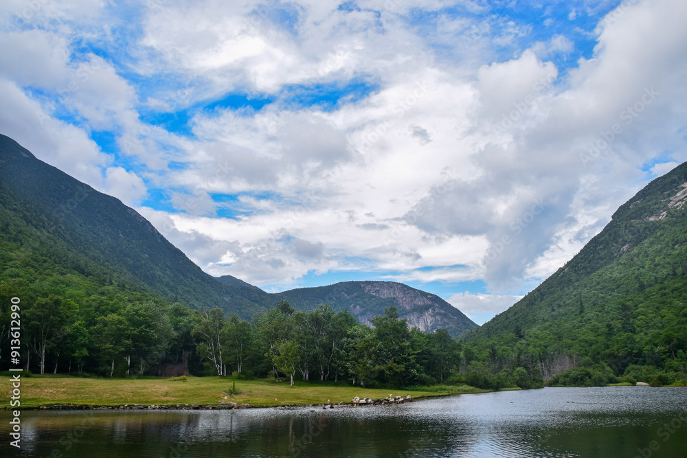 Serene lake surrounded by lush green mountains and a blue sky. Serene lake surrounded by lush green mountains and a blue sky.