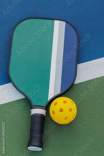 Pickleball paddle and yellow ball on green and blue court.