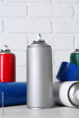 Cans of spray paint on wooden table near white brick wall