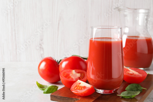 Tasty tomato juice in glass, basil leaves and fresh vegetables on light grey table. Space for text