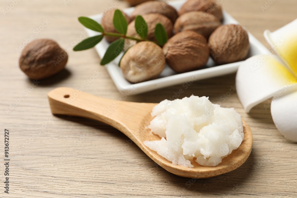 Shea butter in spoon, flower and nuts on wooden table, closeup Shea butter in spoon, flower and nuts on wooden table, closeup