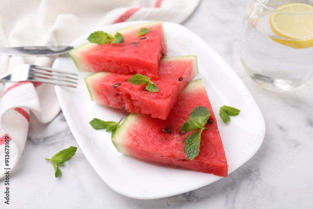 Fresh watermelon slices with mint leaves and glass of water on white marble table, closeup Fresh watermelon slices with mint leaves and glass of water on white marble table, closeup