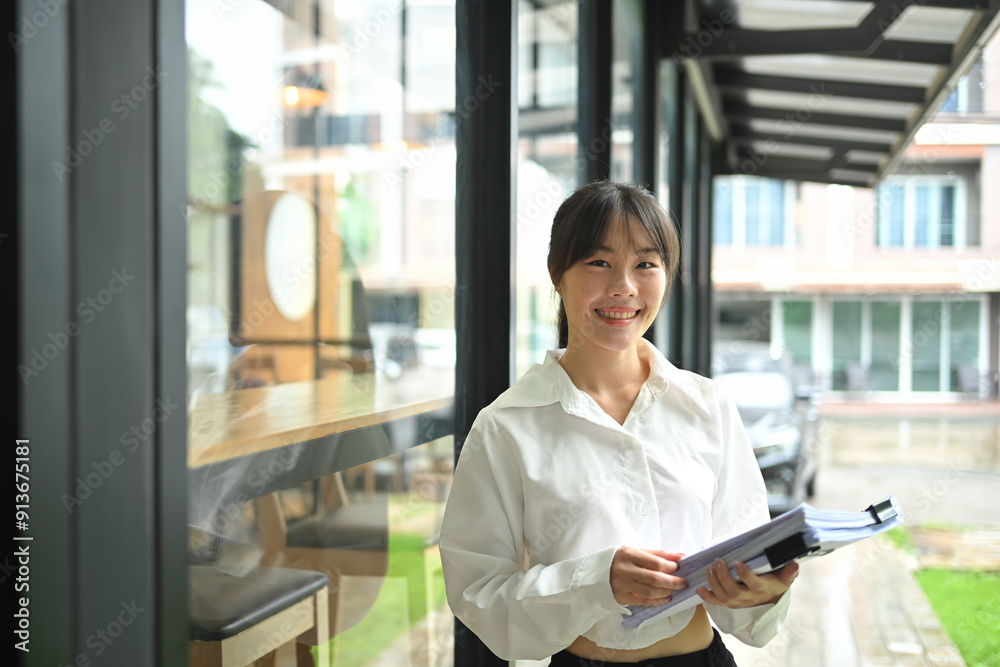 Portrait of a smiling young businesswoman holding document standing outside office building Portrait of a smiling young businesswoman holding document standing outside office building