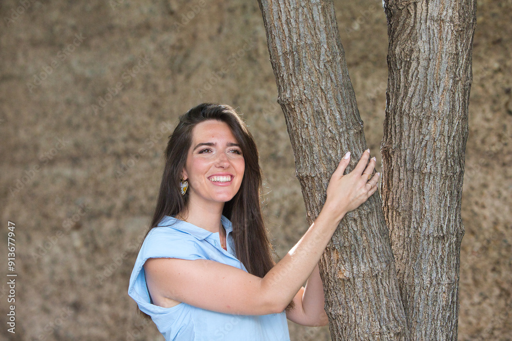 young and beautiful latin woman, clinging to a tree smiles and looks at different places, the woman looks around and is happy in the city she is on holiday. young and beautiful latin woman, clinging to a tree smiles and looks at different places, the woman looks around and is happy in the city she is on holiday.