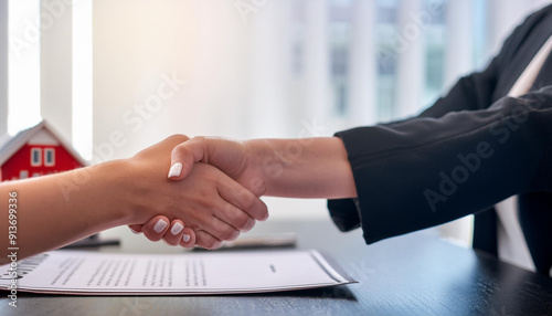 side view of real estate agent and client handshake with miniature house on background