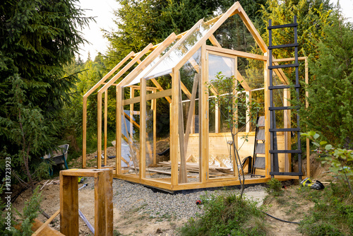 Obraz na płótnie A wooden greenhouse under construction in a lush backyard surrounded by tall trees. The scene captures the early stages of a DIY project in an eco-friendly environment, highlighting sustainable living w salonie