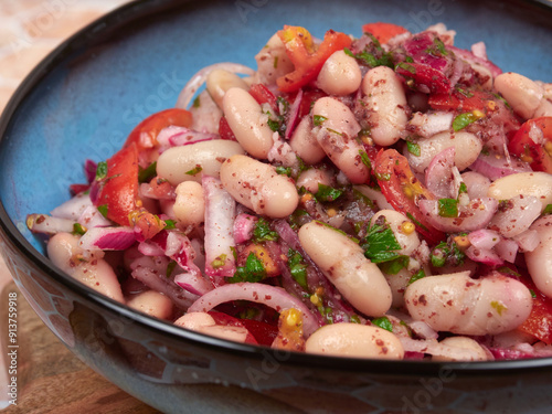 A healthy and nutritious Turkish Piyaz salad featuring white beans, tomatoes, onions, parsley, and sumac. This vegan and vegetarian dish is served in a blue bowl on a wooden board photo