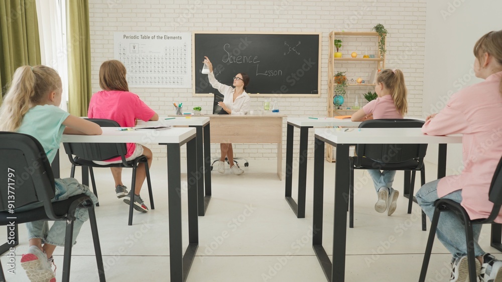 Junior school children sit in classroom on science chemistry lesson. Teacher shows chemical experiment, puts powder in liquid. Modern education concept. Junior school children sit in classroom on science chemistry lesson. Teacher shows chemical experiment, puts powder in liquid. Modern education concept.