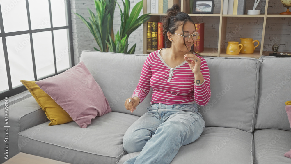 A young hispanic woman relaxes on a sofa in a cozy living room, reflecting a casual and comfortable home environment. A young hispanic woman relaxes on a sofa in a cozy living room, reflecting a casual and comfortable home environment.