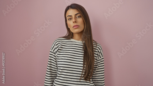 Portrait of a beautiful young hispanic woman in a striped shirt posing against a pink wall, looking thoughtful.