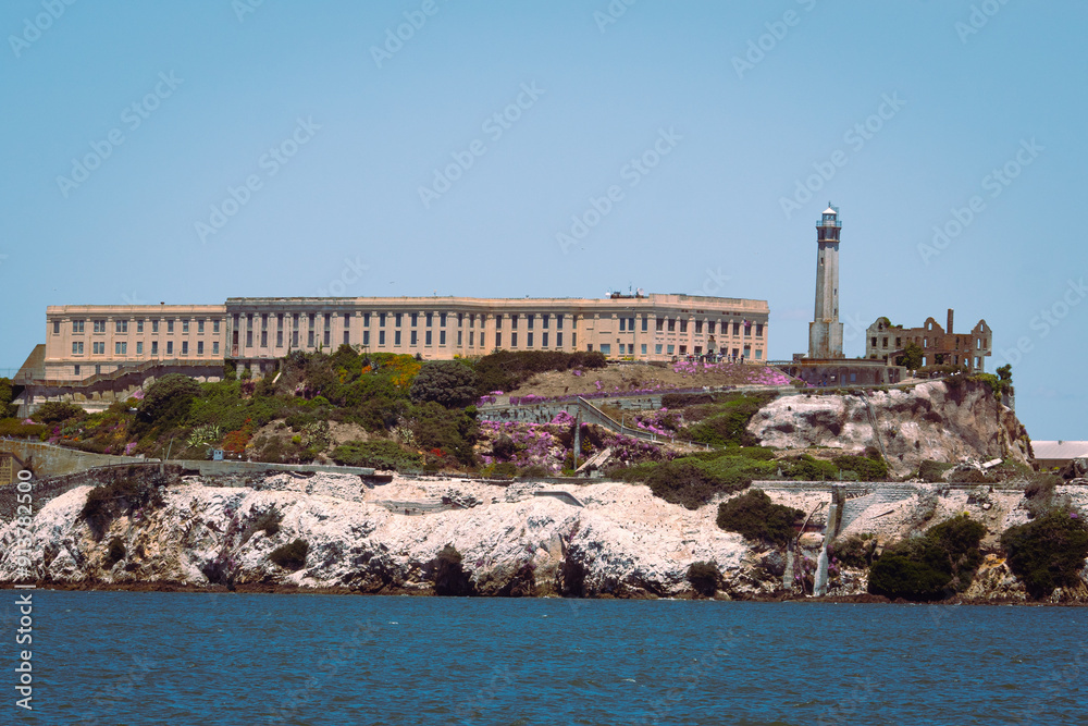 Fototapeta premium Alcatraz Island with its iconic prison and lighthouse surrounded by greenery and rocky terrain. The second image is a black and white photo of the Golden Gate Bridge with hills in the background. The