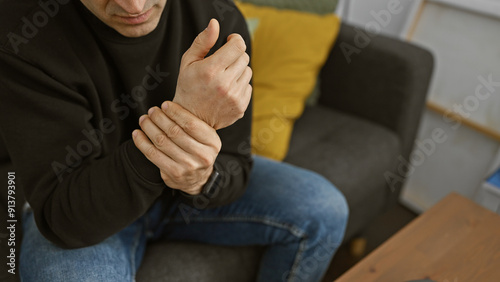 Man suffering from wrist pain while sitting on a couch at home, indicating discomfort and health issues.
