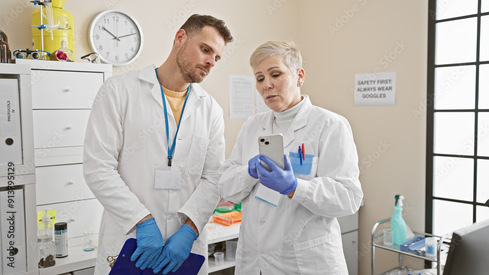 Man and woman scientists in lab coats analyze data on a smartphone in an indoor laboratory setting Man and woman scientists in lab coats analyze data on a smartphone in an indoor laboratory setting